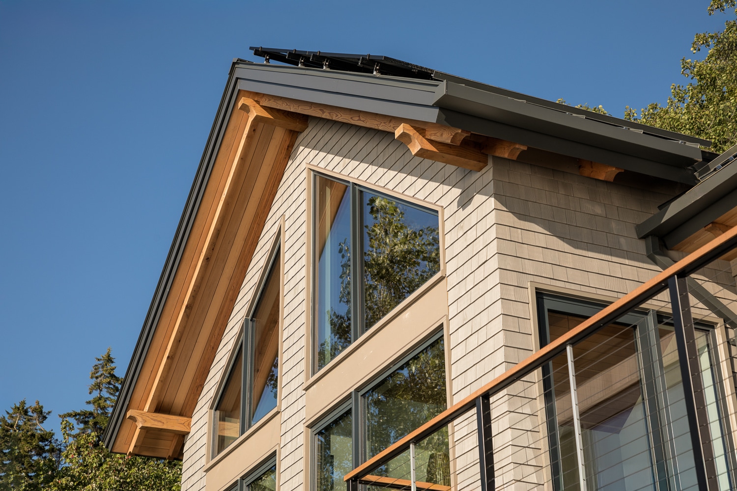 Close-up of a luxury custom home's cedar shingle siding, standing seam metal roof, exposed timber eaves, and rooftop solar panels in Maine by Warren Construction Group.