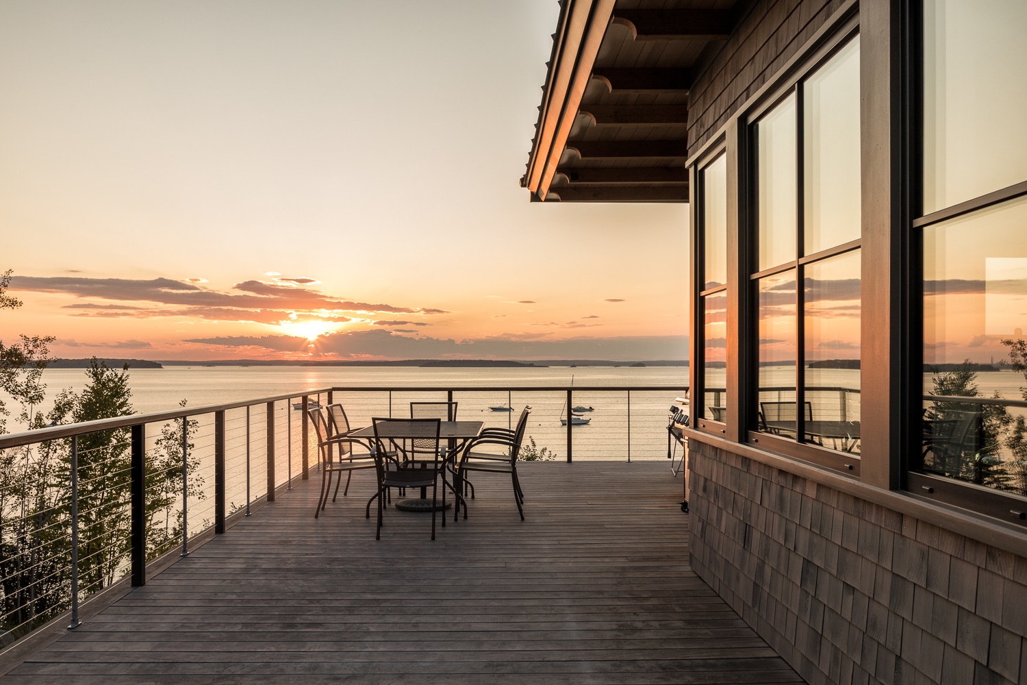 Sunset in Harpswell, Maine from the custom waterfront deck overlooking Casco Bay with cable railings, cedar siding, and outdoor living space built by Warren Construction Group.