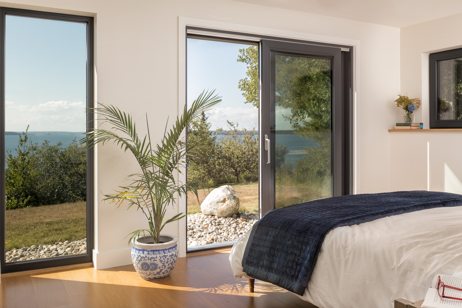 Luxury bedroom in a custom waterfront home with floor-to-ceiling windows, glass door, and panoramic ocean views built by Warren Construction Group.