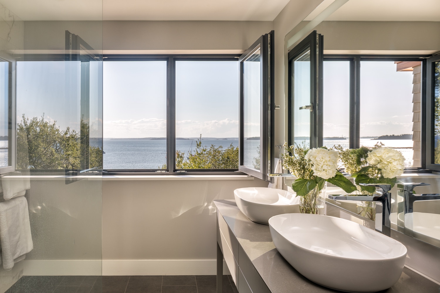 Luxury bathroom with double vessel sinks, large picture windows, and panoramic ocean views in a custom waterfront home built by Warren Construction Group.
