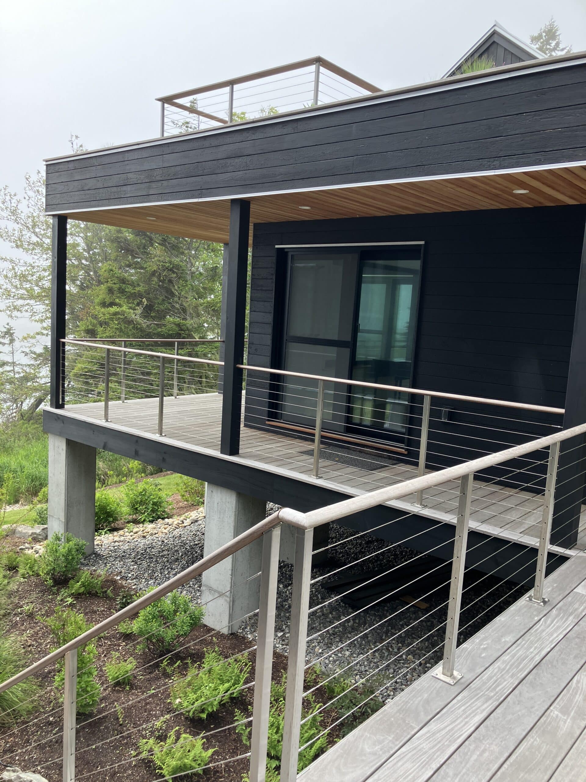 Guest house is raised up on concrete piers to keep it out of the flood plain. Charred siding, stainless steel railing and an ipe deck make this coastal Maine house the perfect retreat.